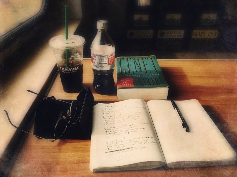 stylized photograph of a journal with pencil, a pair of eyeglasses, a copy of Jean-Paul Sartre's Saint Genet, a Starbucks cold drink cup, and a 20-oz. bottle of Diet Coke on a tabletop